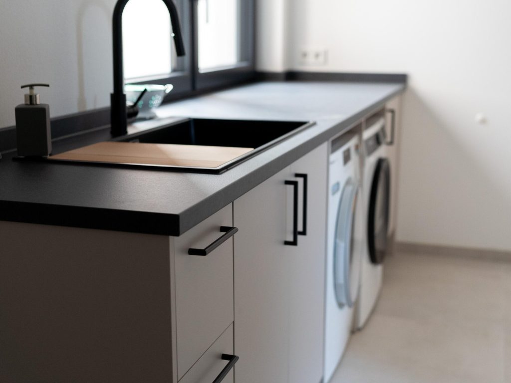 Hauswirtschaftsraum mit Spüle, dunkler Arbeitsplatte und Waschmaschine – Schreinerei Niederreiter