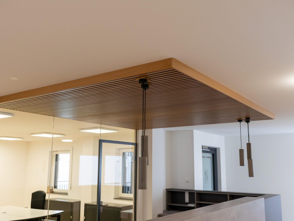 Deckensegel aus Holzlamellen über dem Empfangsbereich eines Büros – Schreinerei Niederreiter